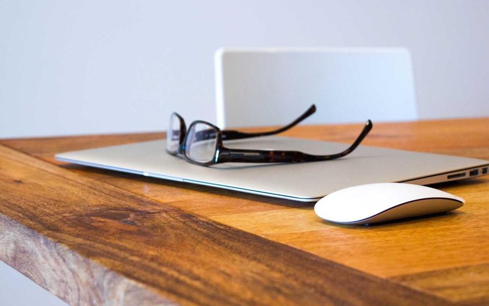 Et skrivebord med laptop, briller og noen notater